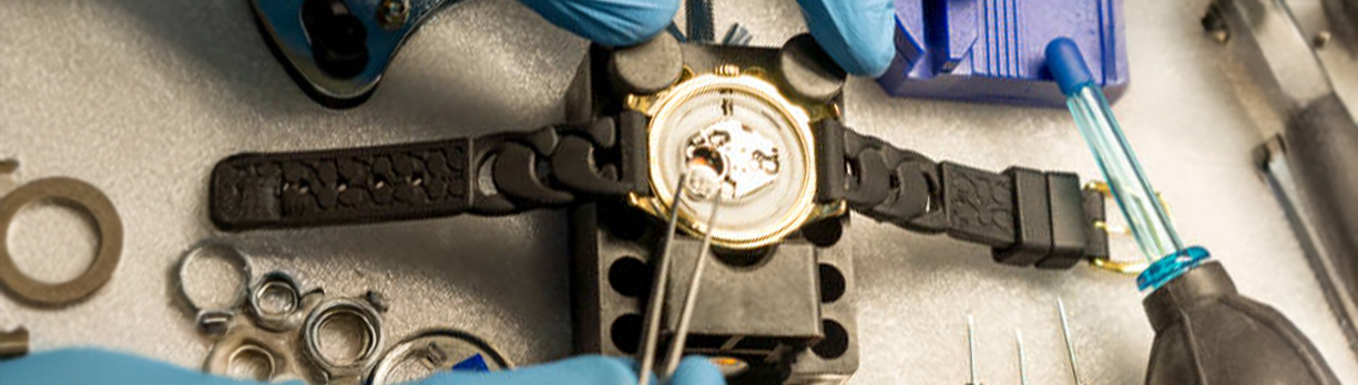 Watch battery replacement with tools and gloves on repair bench