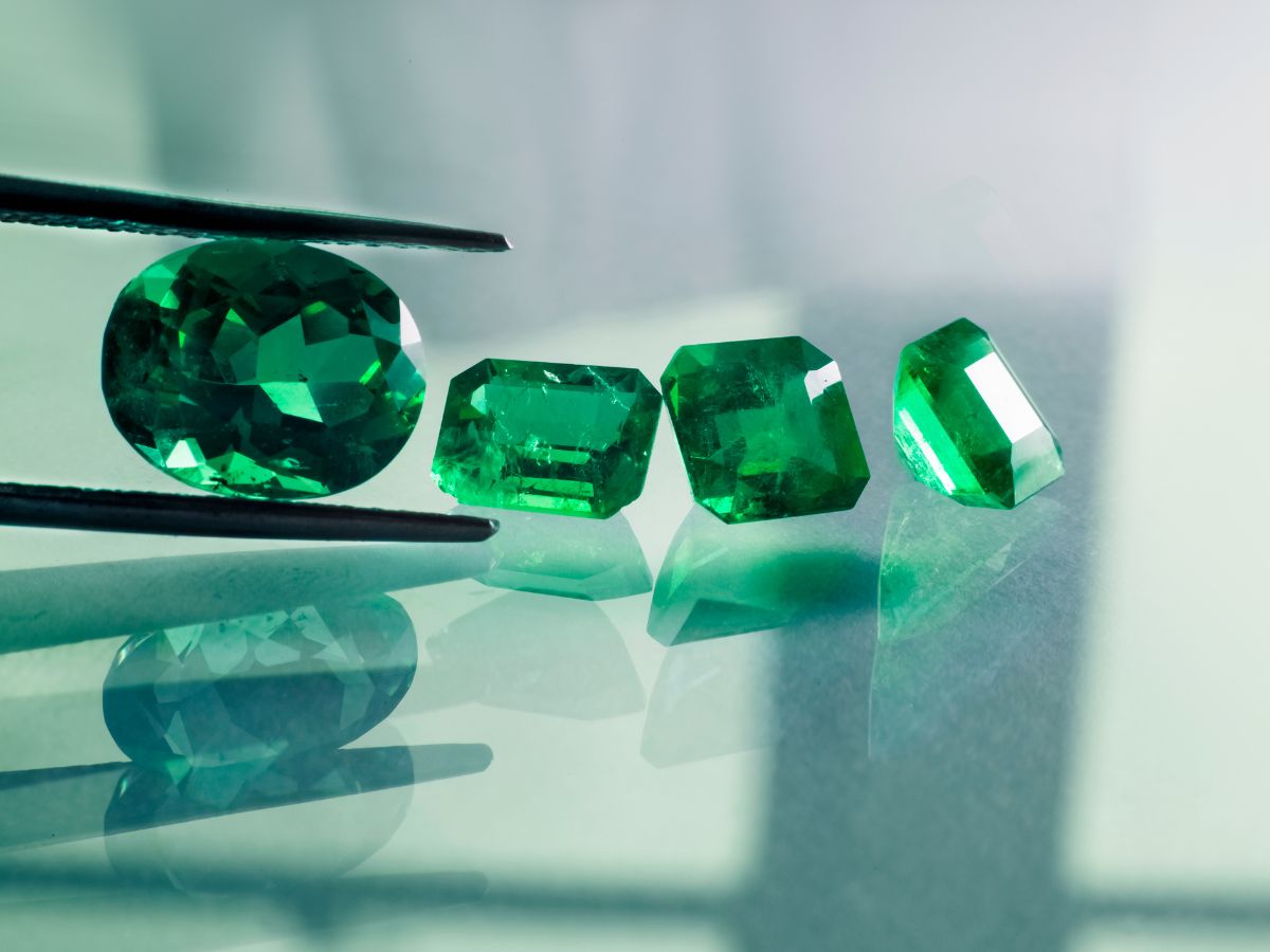 Loose green emeralds held by black tweezers