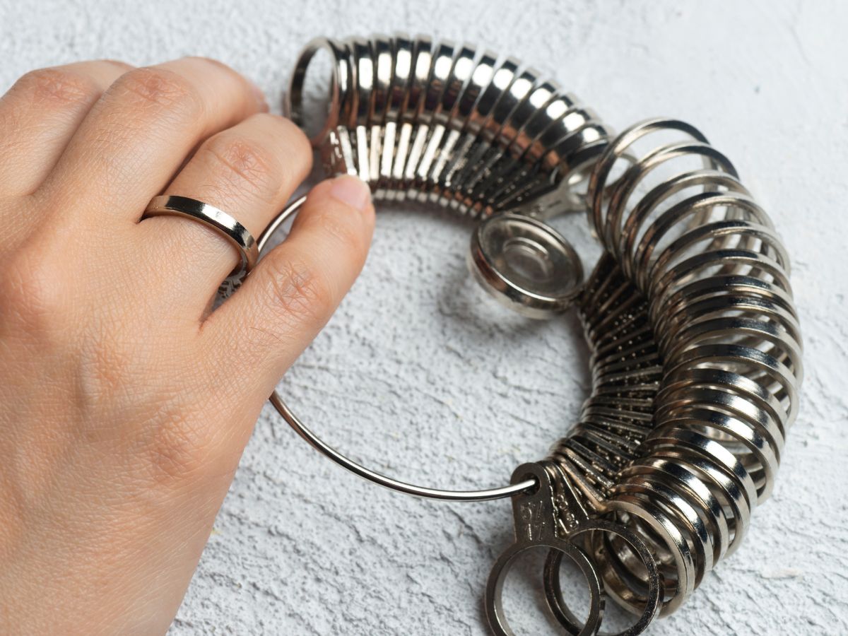 Hand wearing ring next to metal ring sizer on textured table