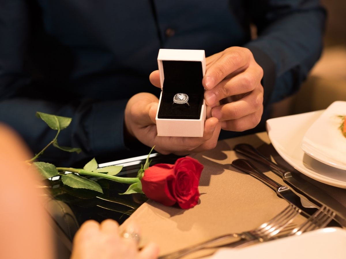 Man proposing with diamond ring at romantic dinner with red rose