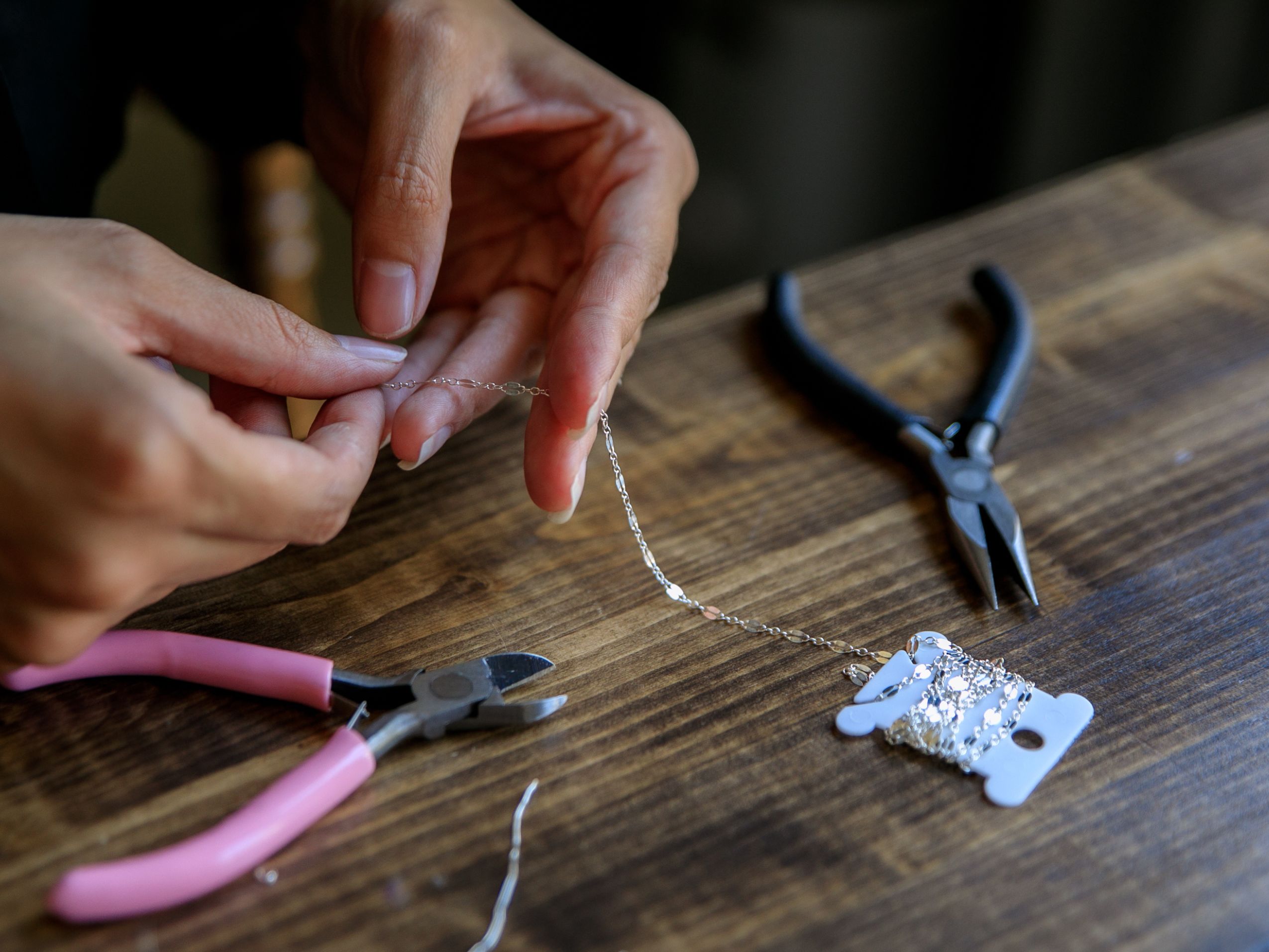 Close-up of hands repairing silver chain jewelry on wooden crafting table