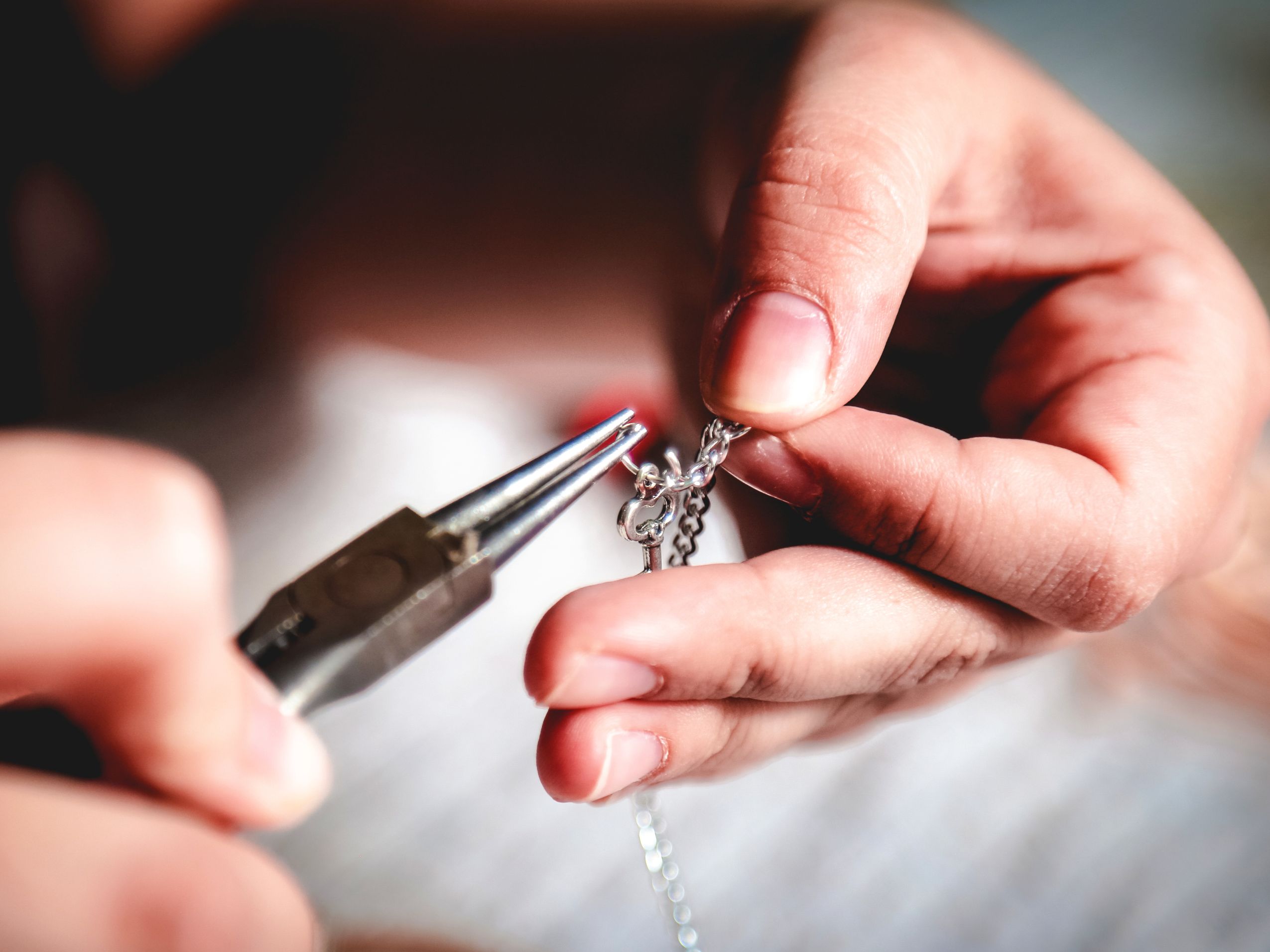 Close-up of hands repairing silver chain jewelry