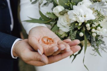 Bride and groom holding wedding bands with white bouquet