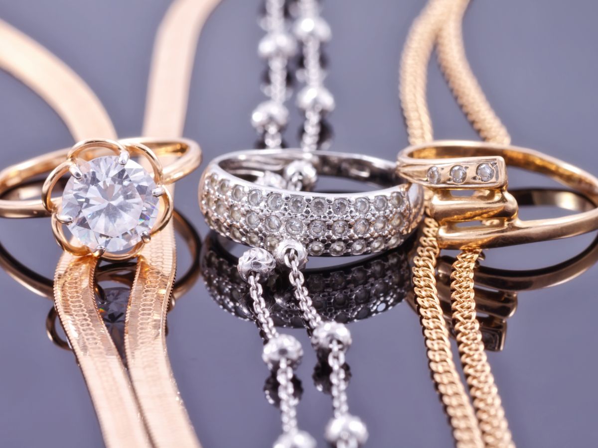 Yellow gold, rose gold, and white gold diamond rings with necklaces on reflective black surface.