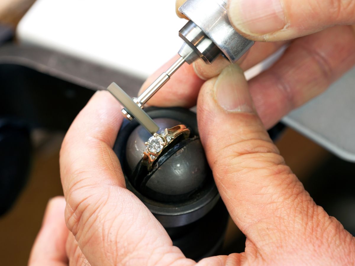 Jeweler polishing diamond ring with rotary tool close-up view.