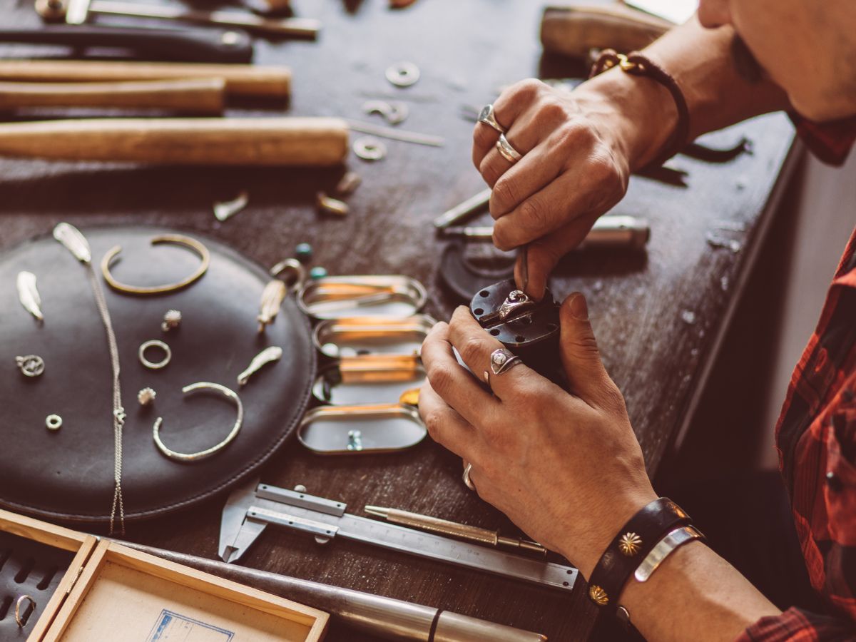 Craftsman performing jewelry repair at cluttered workbench table.