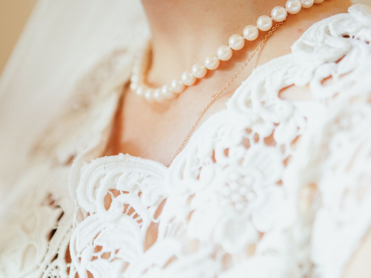 Close-up of bride’s pearl necklace and detailed white lace wedding dress.