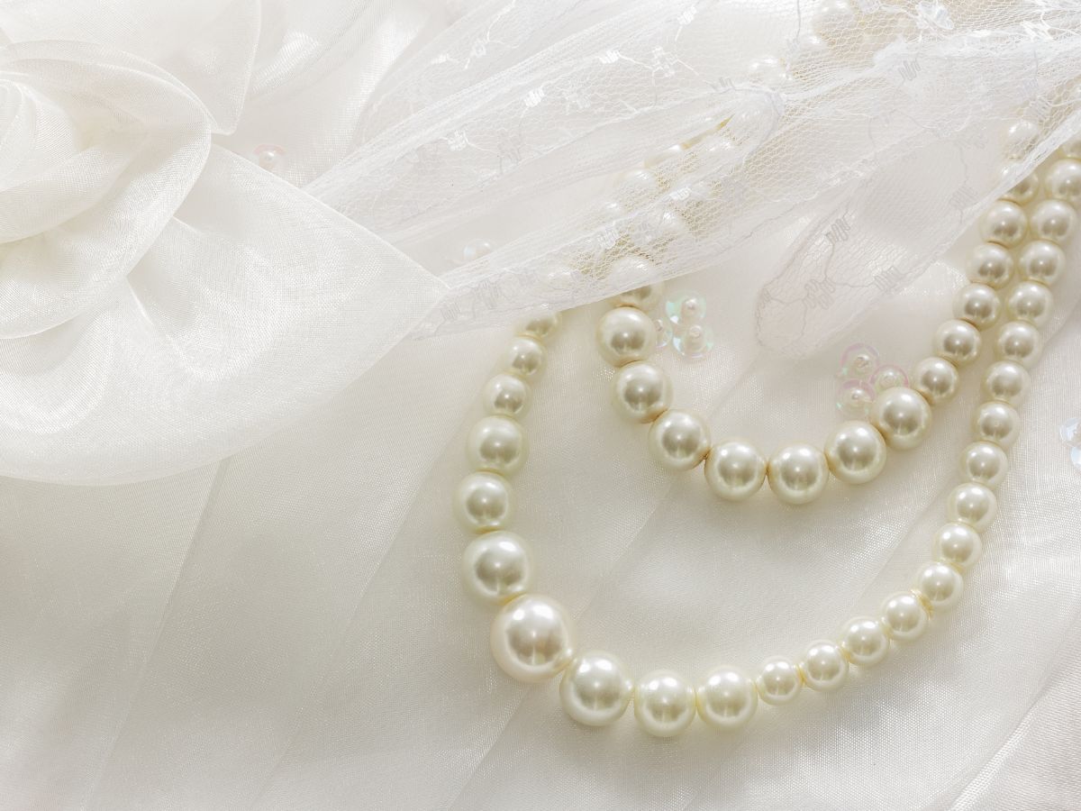 Pearl necklace on white satin with lace and sequins, elegant wedding detail.