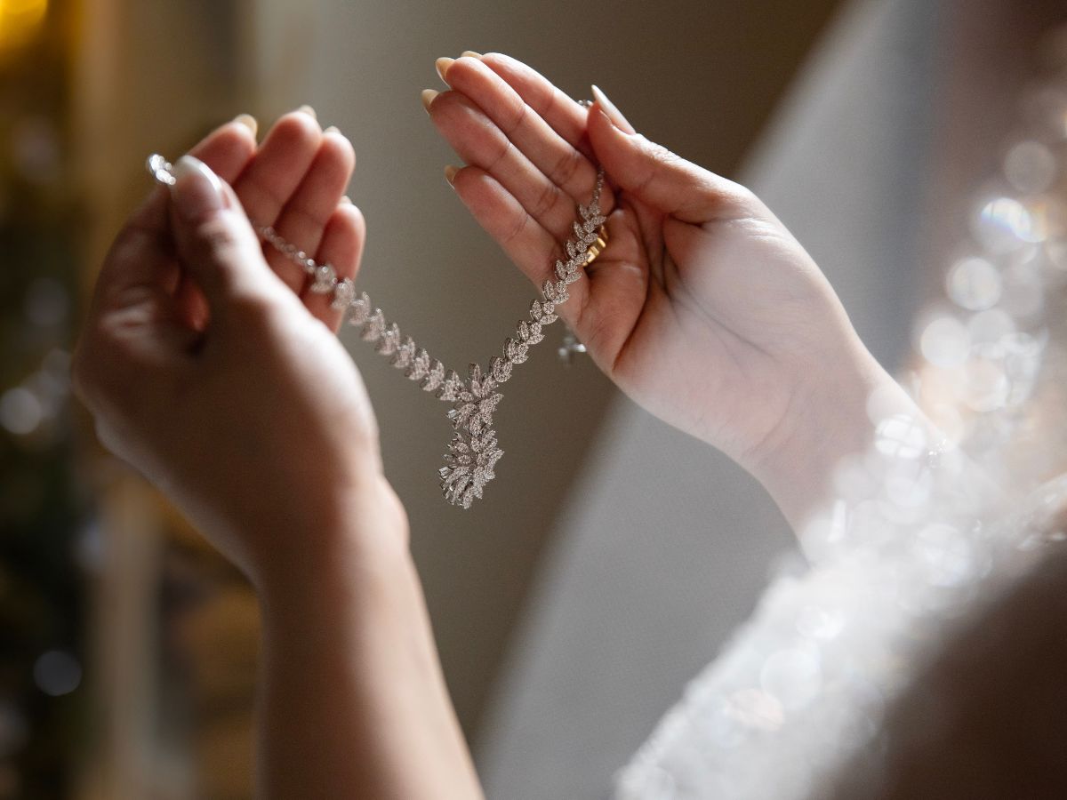 Bride holding sparkling diamond necklace with leaf design in soft light.