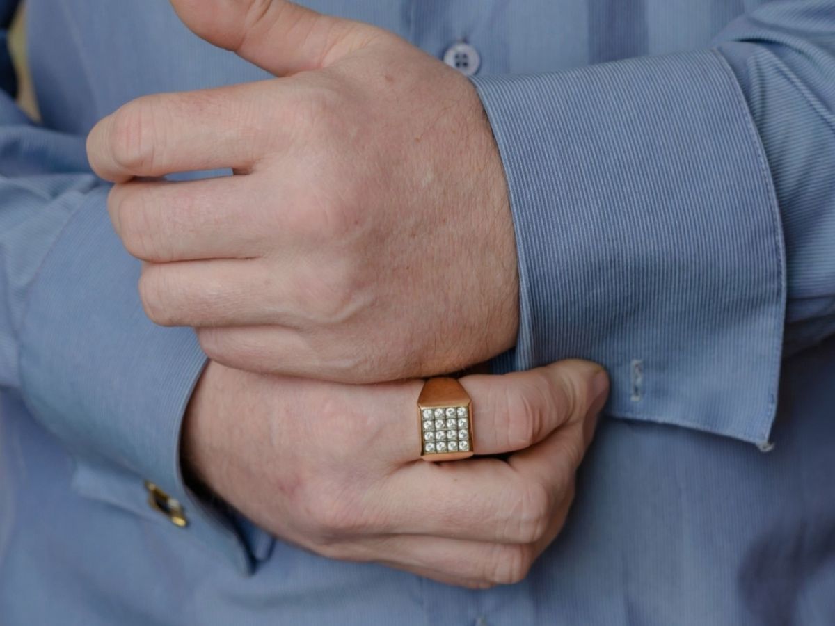 Man in blue shirt wearing square signet gold ring with rows of small diamonds.