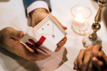 Man gifting diamond jewelry set in box, romantic candlelight setting.