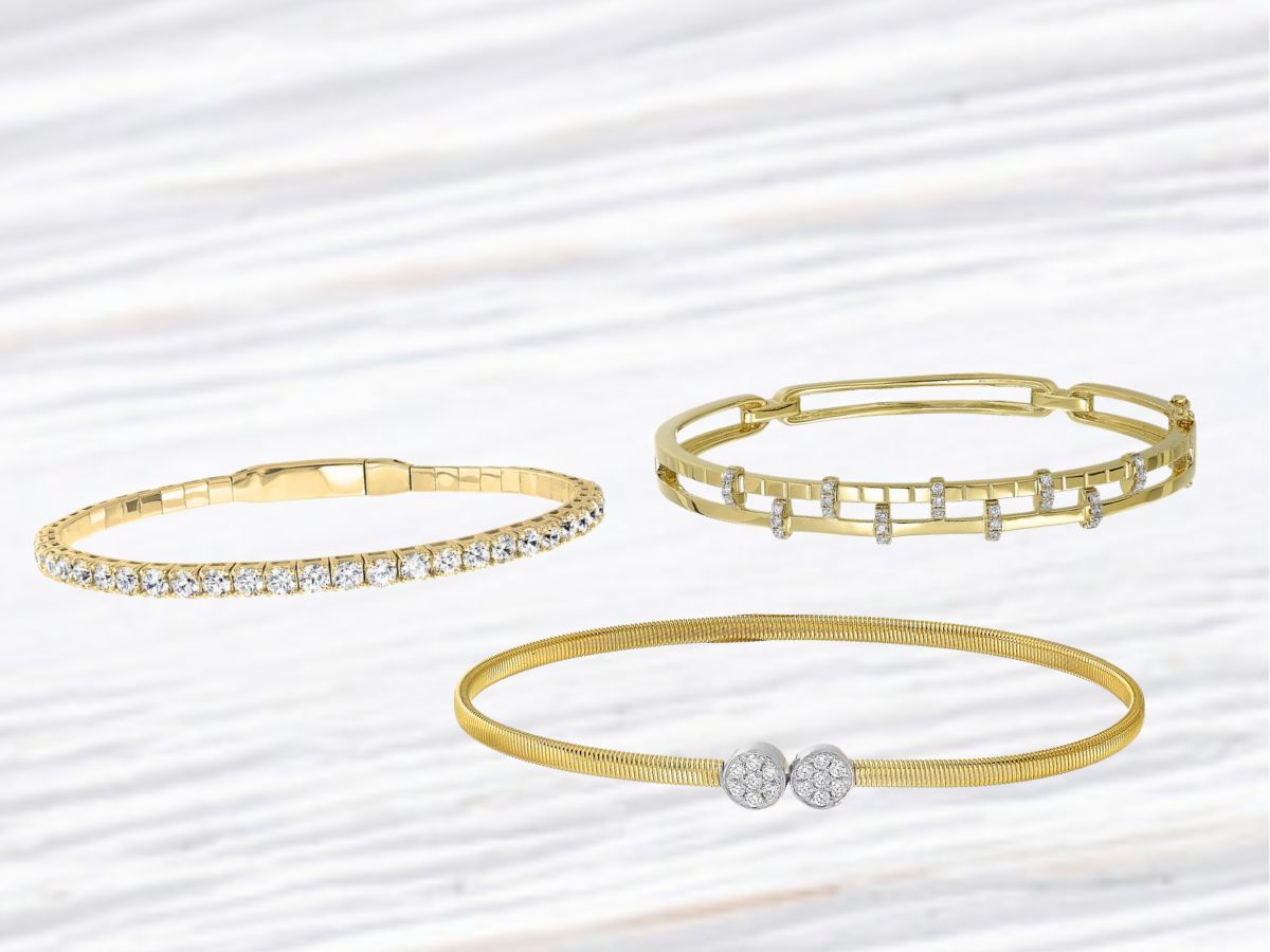 Trio of stylish gold bangles with diamond accents on white wood background.