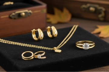 A collection of yellow gold jewelry, including a necklace, hoop earrings, and a diamond ring, displayed on a black velvet tray next to a wooden jewelry box.