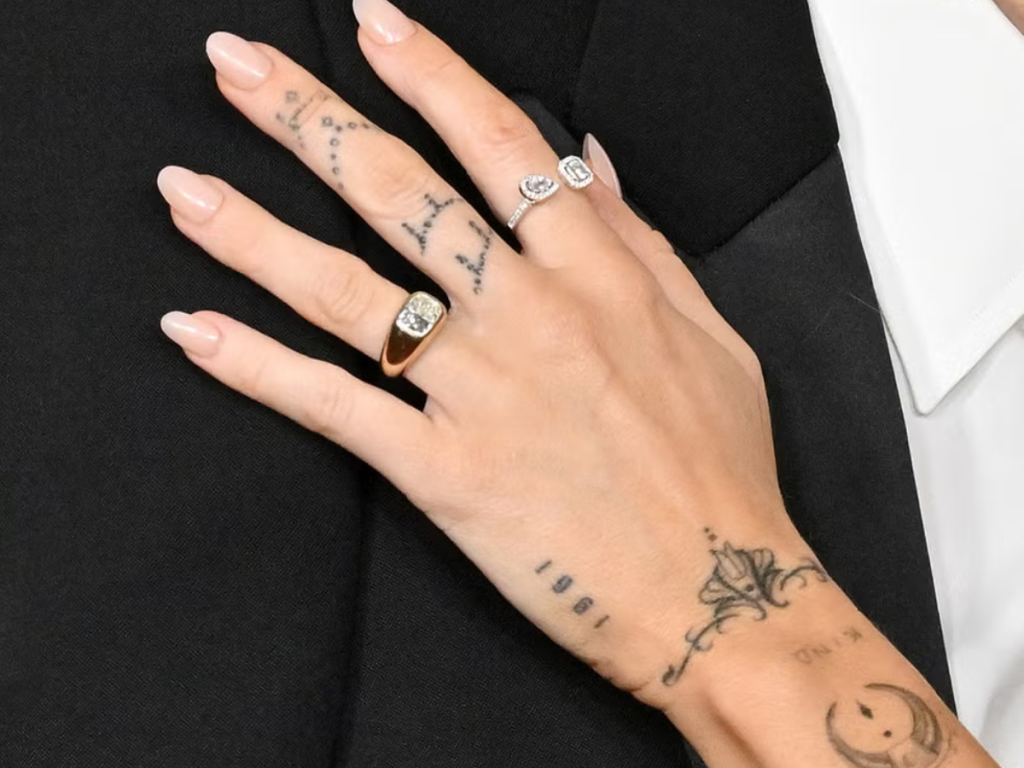 Gold diamond statement engagement ring stacked with delicate diamond band on tattooed hand.