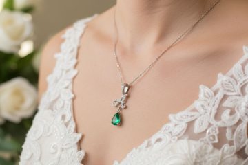 A bride wearing a delicate silver necklace with an initial pendant and a green gemstone.