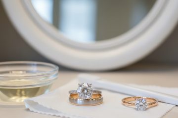 Two bridal rings, a small bowl of cleaning solution, and a soft cloth on a vanity.