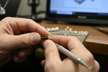 A jeweler's hands carefully working on a ring, setting a small gemstone with tools.