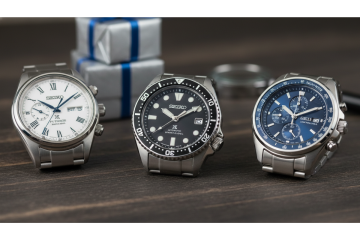 Three different styles of Seiko watches on a wooden surface with a gift box in the background.