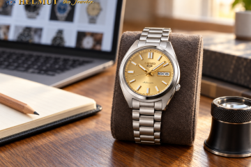 Gold-dial Seiko automatic watch on a desk beside a laptop