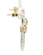 A close-up side view of a silver huggie hoop earring with a textured drop charm and gold post, shown on a white background.