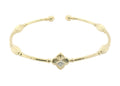 A delicate yellow gold open cuff bracelet featuring a central quatrefoil flower motif with a small clear gemstone, accented by ribbed bead details along the band.