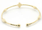 A gold-toned metal cuff bracelet with a beaded, segmented design and a small diamond-shaped charm at the top, photographed on a plain white background.
