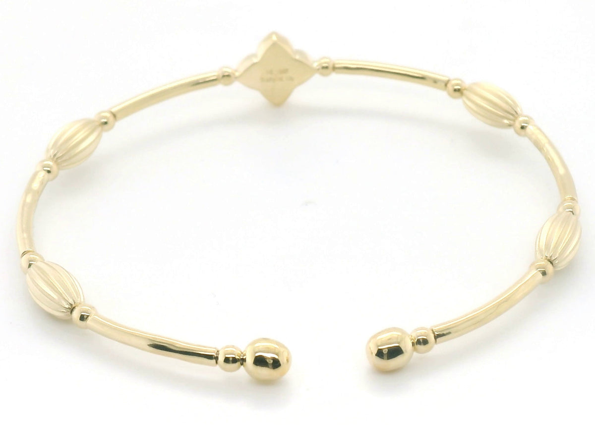 A gold-toned metal cuff bracelet with a beaded, segmented design and a small diamond-shaped charm at the top, photographed on a plain white background.